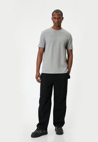 Vaaleanharmaa lyhythihainen t-paita pyöreällä pääntiellä, yhdistettynä mustiin cargo-housuihin, joissa on useita taskuja ja rento istuvuus.