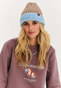 Kolorowa czapka dziana z beżową górą i jasnoniebieskim prążkowanym paskiem. Posiada małą bordową metkę. Noszona z brązową bluzą.