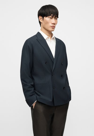 Σκούρο μπλε διπλόκομπο σακάκι από δομημένο ύφασμα με γιακά με εγκοπές, διαθέτει δύο μπροστινές τσέπες και κουμπιά σε αντίθεση.