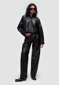 Zwart leren cropped shirt met knoopsluiting en borstzak, gecombineerd met zwarte leren high-waisted broek en puntenlaarzen.