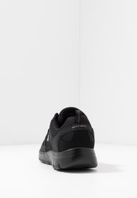 Černá atletická bota s horní částí z prodyšné síťoviny, polstrovanou podešví a úchopovým jazykem na patě. Nabízí hladký, zaoblený tvar a texturované prvky.