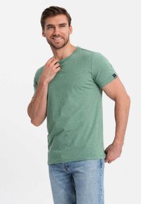 Camiseta verde jaspeada de tejido suave, con cuello redondo, mangas cortas, con motas de diferentes tonalidades y un pequeño parche de logo en la manga.