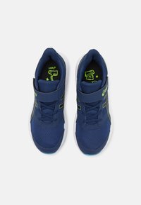 Baskets de sport bleu marine avec une tige en mesh, accents verts contrastants, une sangle Velcro et une semelle en caoutchouc blanche. Présente des détails texturés.