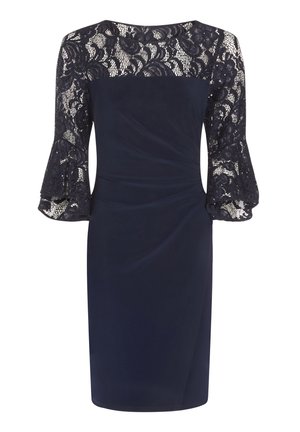 Granatowa sukienka do kolan z koronkową góra i rękawami, rozkloszowanymi koronkowymi mankietami oraz drapowanymi zdobieniami z przodu.