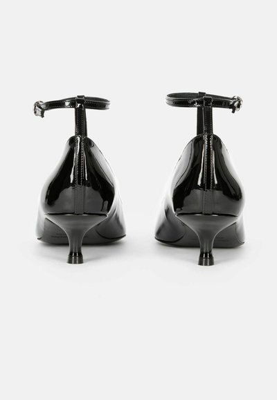 Talons en cuir verni noir avec un bout pointu, une fine bride à la cheville et un talon aiguille modéré. Surface lisse et brillante.