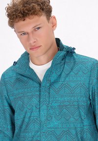 Türkise Jacke mit geometrischem Muster, seitlichen Taschen, verstellbarem Kapuzen und einem Reißverschluss vorne. Hergestellt aus leichtem Material.