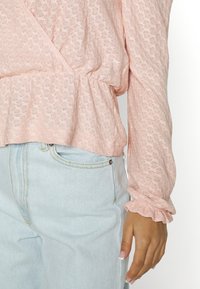 Ljusrosa, texturerad långärmad topp med en inslagning och volangärmar, i kombination med ljusblå jeans med en framficka.