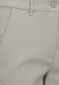 Lichtgrijze broek met een gestructureerde stof, platte voorkant, zijzakken en een knoopsluiting, met een zichtbare naaddetail.