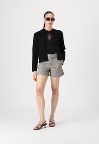 Μαύρο πλεκτό καρό με στρογγυλή λαιμόκοψη, γκρίζες καρό κομμένες σορτς, και μαύρες στριφτές γόβες, σε συνδυασμό με oversized γυαλιά ηλίου.