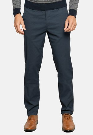 Pantalones azul marino de tela ligera, con un corte ajustado, detalles de costura visibles y una textura suave, acompañados de zapatos marrones con cordones.