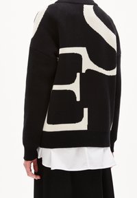 Czarny sweter dzianinowy z dużym kremowym nadrukiem, o luźnym kroju, z prążkowanymi mankietami i widocznym, warstwowym dolnym wykończeniem.