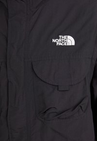 Sort jakke-lomme med klap og sort hængeløkke, der har et hvidt broderet "The North Face" logo på stoffet.