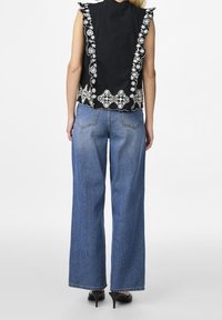 Haut noir sans manches avec broderie florale blanche sur l'ourlet et les emmanchures, associé à un jean large bleu taille haute et des talons noirs.