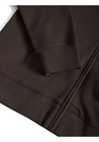 Brun sweatshirt med en texturerad yta, som har en åtsittande ärm och synliga sömmar. Inkluderar en liten ficka på sidan.