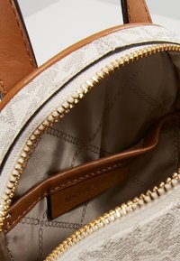 Interno di una borsa Michael Kors, con accenti in pelle beige, cerniera dorata e un tessuto chiaro con un sottile motivo a catena.