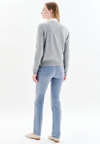 Maglione grigio chiaro con una finitura testurizzata, abbinato a jeans azzurri chiari. Scarpe piatte beige e dettagli minimalisti sul maglione.