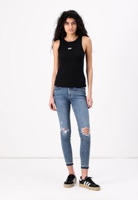 Fekete ujjatlan felső, rajta a "GAP" logóval, kék skinny farmernadrággal, amelyen elnyűtt szakadásokat találunk, és fekete sportcipőkkel, fehér csíkokkal és bézs talppal.