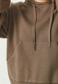 Brown hoodie made of soft fabric, featuring a front pocket, drawstrings at the neck, and ribbed cuffs and hem. Mid-length cut.