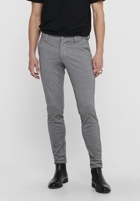 Pantalon ajusté gris en tissu léger, avec devant plat, fermeture boutonnée et poches latérales, assorti à des bottines noires.