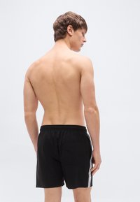 Μαύρο μαγιό κοντό με ελαστική μέση, πλευρικές ρίγες και πίσω τσέπη. Το υλικό φαίνεται ελαφρύ και λείο.