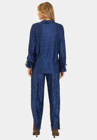 Conjunto de pijama de satén azul marino con un patrón texturizado de diamantes. La parte superior tiene mangas largas con lazos, y los pantalones cuentan con aberturas en el dobladillo.