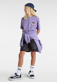 Fialová košile s logem Vans, šedé a černé kostkované šortky, bílé ponožky s textem Vans, černé boty a modrá kšiltovka. Neformální outfit.