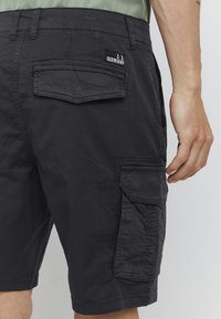 Shorts cargo noirs en coton avec plusieurs poches, présentant une finition texturée et une étiquette de logo sur la poche arrière.