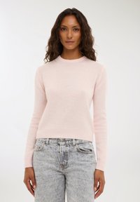 Maglione rosa chiaro realizzato in morbido materiale, con scollatura rotonda e orlo a costine. Indossato sopra jeans chiari, leggermente strappati.