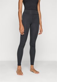 Leggings noirs en tissu extensible, design ajusté avec une taille haute, texture lisse et détails de couture minimaux.