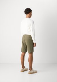 Olive green shorts with an elastic waistband, paired with a white long-sleeve shirt and beige sneakers with light gray accents.