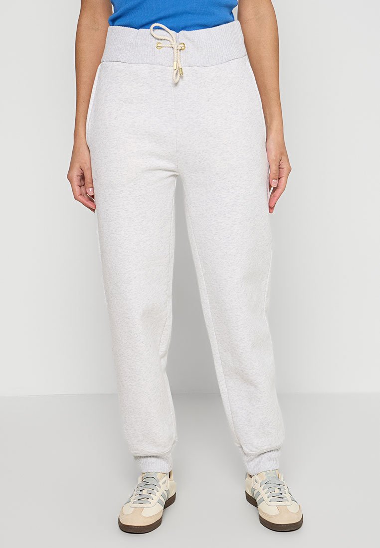 Pantalones de chándal grises claros con cintura elástica, cordón ajustable, tobillos acampanados y una tela suave y texturizada. Combinados con zapatillas beige.