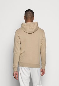 Felpa con cappuccio in cotone color beige con coulisse, caratterizzata da maniche lunghe e orlo dritto. Tessuto liscio, senza motivi o dettagli visibili.