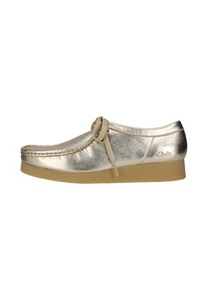 Metallic goldfarbener Leder-Mokassin-Schuh mit beigen Schnürsenkeln und hellbrauner Krepsohle, Seitenansicht, mit Clarks-Logo an der Ferse.