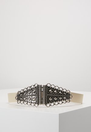 Elastisk beige bælte med en udsmykket mørk sølvspænde med geometriske og cirkulære dekorative elementer.