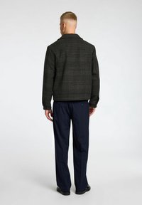 Veste à carreaux noirs avec col et manches longues, associée à un pantalon bleu marine. La veste a une finition texturée et une coupe ajustée.