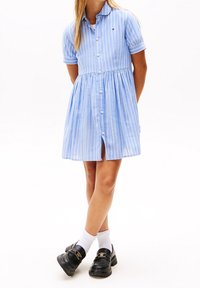 Abito a maniche corte a righe blu e bianche con bottoni sul davanti e gonna a campana. Indossato con scarpe nere e calzini bianchi alla caviglia.