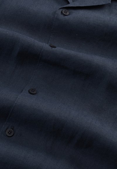 Tissu de chemise en lin bleu foncé avec texture de tissage visible et trois boutons noirs le long de la patte centrale.