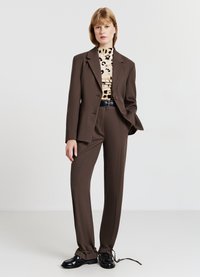 Completo marrone su misura con blazer monopetto, abbinato a un dolcevita con stampa leopardata. Cintura nera e scarpe stringate lucide.