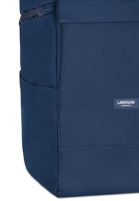 Sac à dos bleu marine en tissu durable, doté d'une poche zippée, d'une poche latérale et d'une forme rectangulaire avec une étiquette de marque.