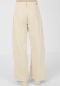 Pantaloni a gamba larga in tessuto beige chiaro con una finitura testurizzata e orlo sfilacciato. Presentano passanti per cintura e un design a vita alta.