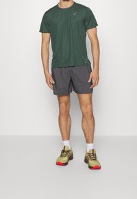 Green short-sleeve athletic t-shirt, black checkered shorts, and tan running shoes with red accents, white socks and a black logo on the shirt.