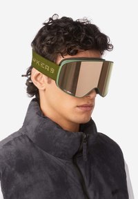 Skibrille mit einem grünen Schaumrahmen, großen verspiegelten Gläsern und einem strukturierten grünen Band mit Text. Wird von einer Person in einer dunklen Jacke getragen.