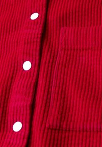 Rotes Cordhemd mit gerippter Textur, weißen Knöpfen und einer Brusttasche. Der Stoff ist weich und plüschig mit vertikalen Streifen.