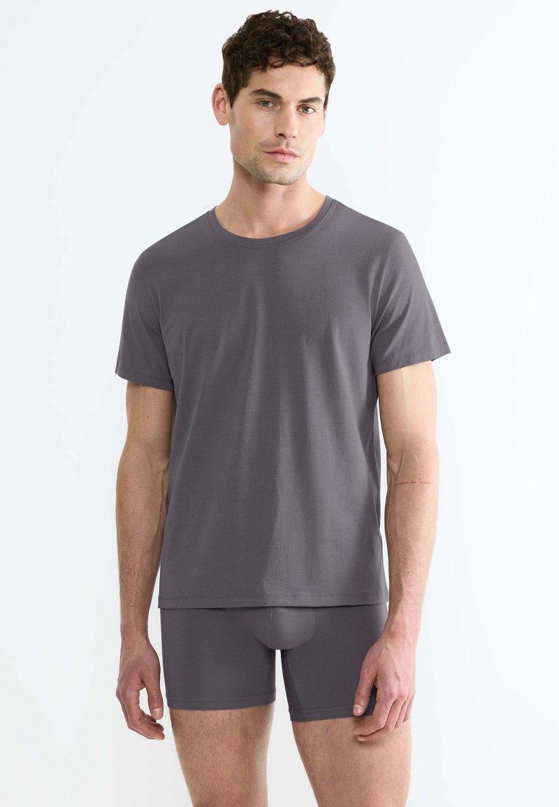 T-shirt grigio in cotone con maniche corte e scollo rotondo, abbinato a pantaloni sportivi grigi in coordinato, caratterizzati da una texture liscia.