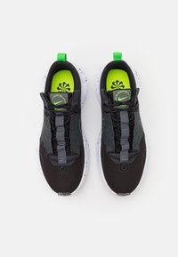 Black athletic sneakers with a textured mesh upper, grey accents, and a vibrant lime green insole. Features a pull tab and lace-free design.