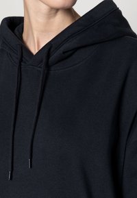 Czarna bawełniana bluza z kapturem o luźnym kroju, z regulowanym kapturem i ściągaczami na mankietach. Gładka faktura bez widocznych wzorów czy akcentów.