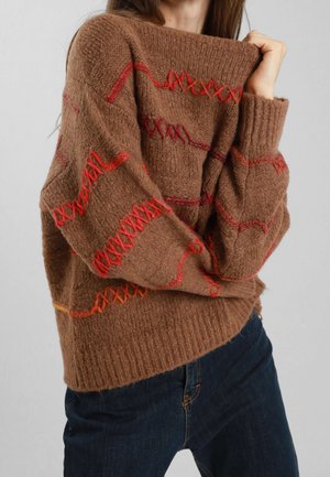 Maglione marrone lavorato a maglia con motivi ricamati rossi, dotato di un ampio scollo e polsini a coste. La texture è morbida e pelosa.