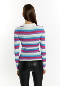 Dryžuotas megztinis su pašiaušta tekstūra violetinės, rožinės, mėlynos ir baltos spalvų, su apykakle ir ilgomis rankovėmis, derinamas su juodomis prigludusiomis kelnėmis.