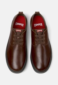 Braune Lederschuhe mit abgerundeter Spitze, flachen Schnürsenkeln und strukturierten Akzenten. Rote Innensohlen mit "CAMPER"-Markenaufdruck. Schwarze Laufsohle.