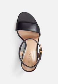 Sandalo in pelle nera con unaampia cinghia alla caviglia, design minimalista, con soletta beige liscia e dettaglio della fibbia dorata.
